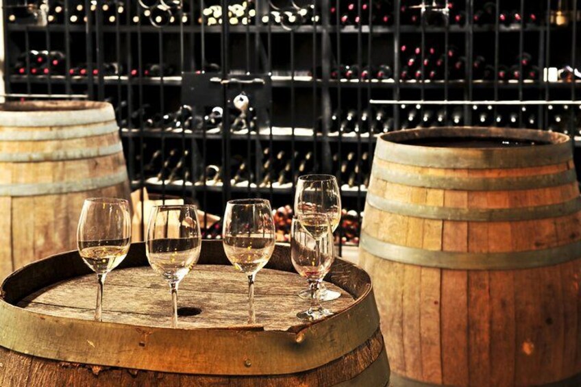 Tres copas de vino sobre un barril de madera, con una botellera al fondo. 1