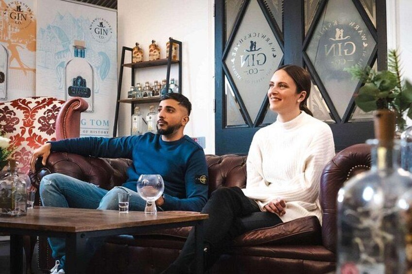 To personer sidder på en lædersofa i et rum med et kort og hylder med flasker. 2