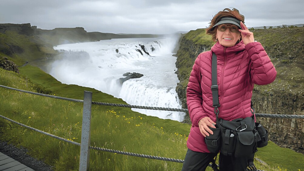 Eine Person steht an einem Wasserfall, im Hintergrund eine felsige Landschaft. 2