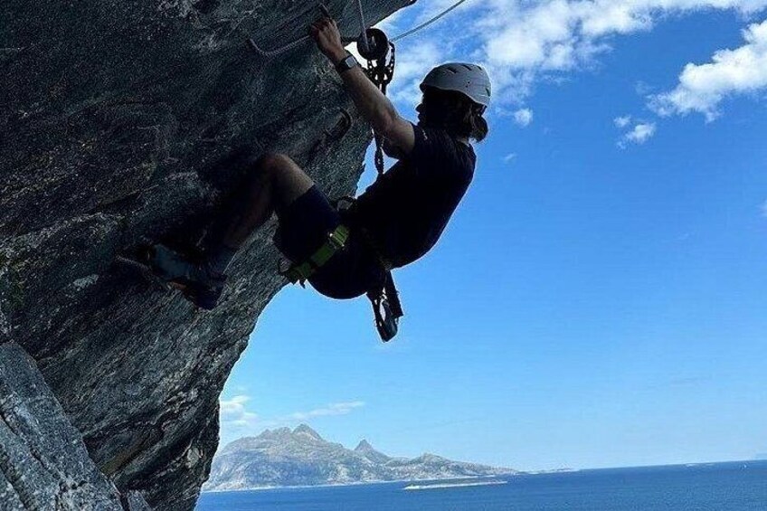 A person rock climbing on a cliff with a clear sky and a distant mountain range. 3