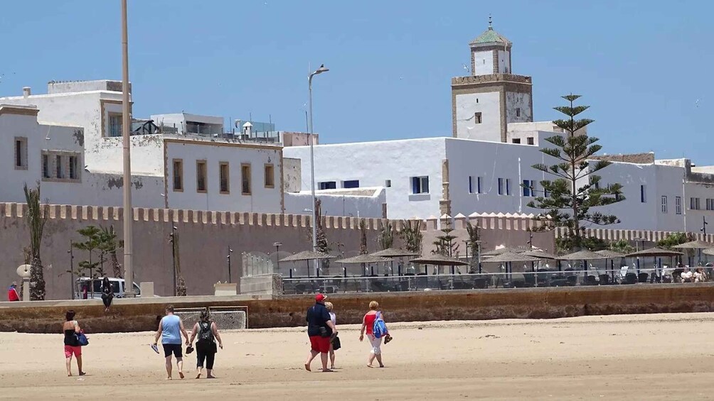 A sandy beach with people walking, a white building with a tower, and a clear blue sky. 4