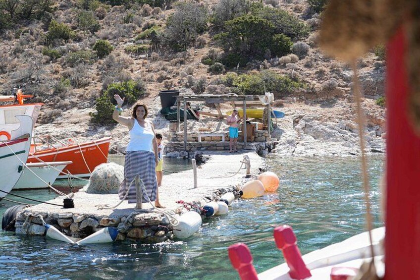 A woman standing on a floating platform in a body of water, with boats and a rocky shoreline in the background. 3