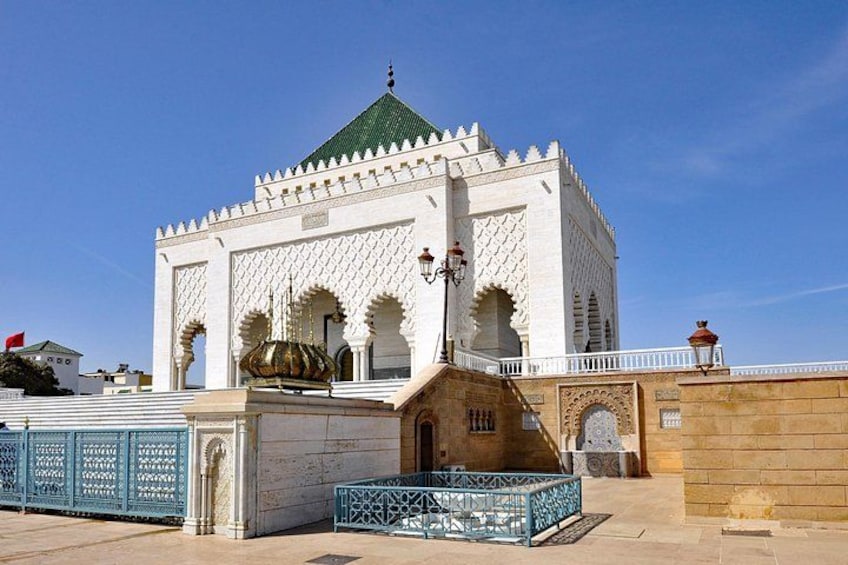 A white mosque with green domes and arches, a blue fence, and a clear blue sky. 1