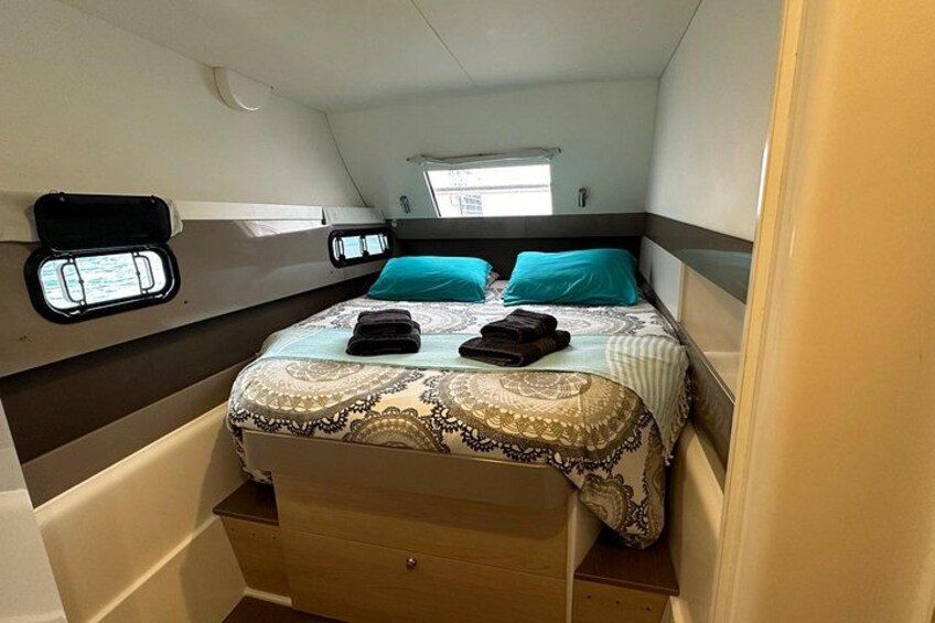 Een knus slaapkamer met een bed, twee kussens, een raam en een klein opbergkastje. 2