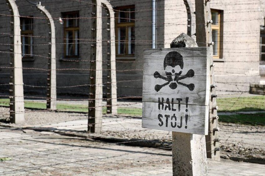 A warning sign with a skull and crossbones and the words 'HALT! STOJ!' in front of a barbed wire fence. 2