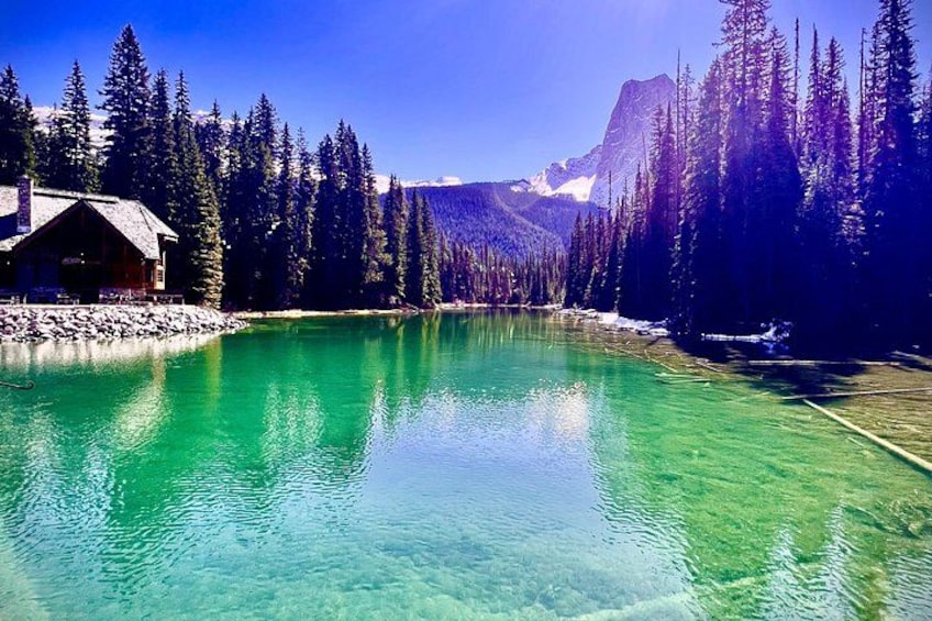 A clear turquoise lake surrounded by dense coniferous forest and a mountain range. 2