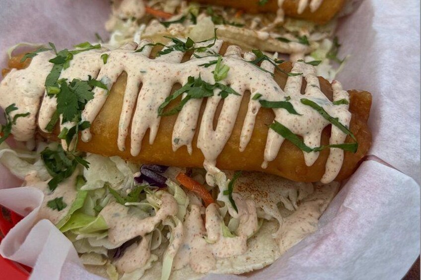 A basket containing spring rolls, a creamy sauce, and a side of mixed salad. 2