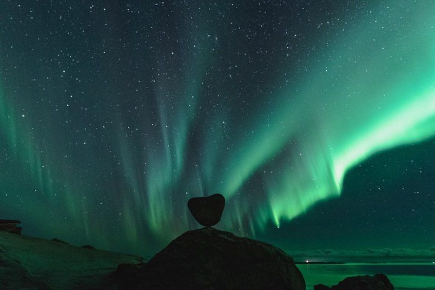 A person sitting on a rock under a starry night sky with the Northern Lights. 3