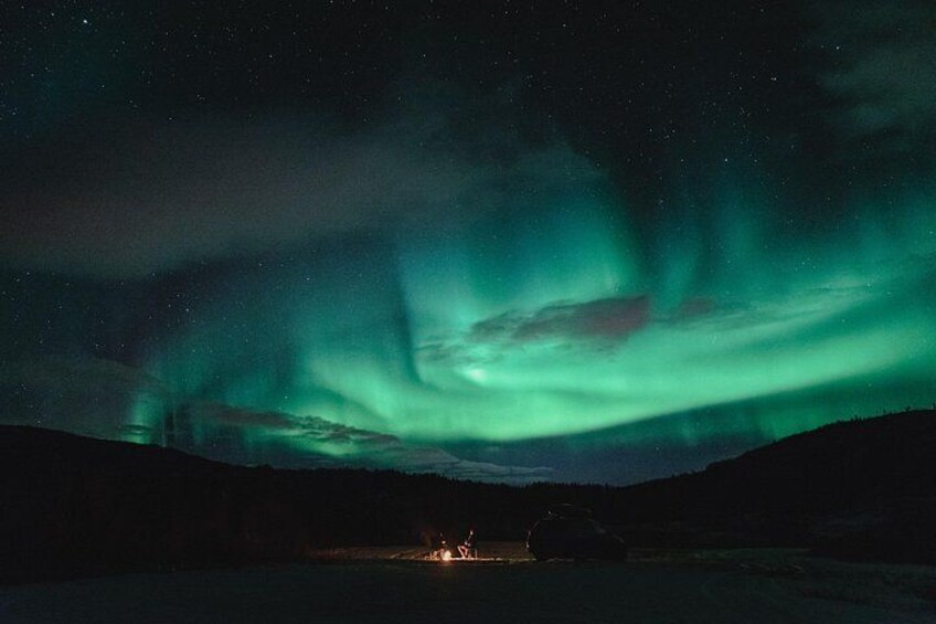 The Northern Lights over a snowy landscape with a distant cabin. 5