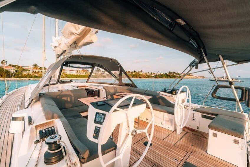 A boat's deck with a steering wheel, control panel, and a view of the water and distant shoreline. 2