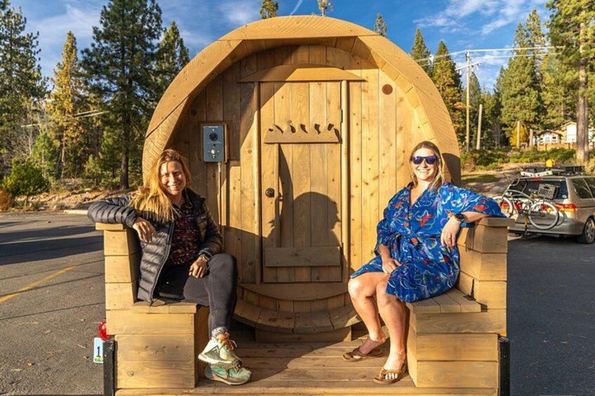 Two people sitting on a wooden bench with a wooden structure behind them. 3