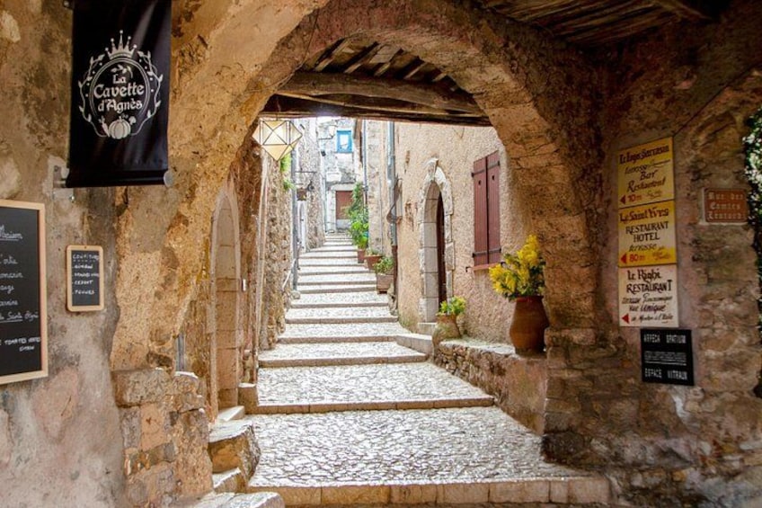 A narrow cobblestone alleyway with stone buildings, a black banner, and a signboard. 2