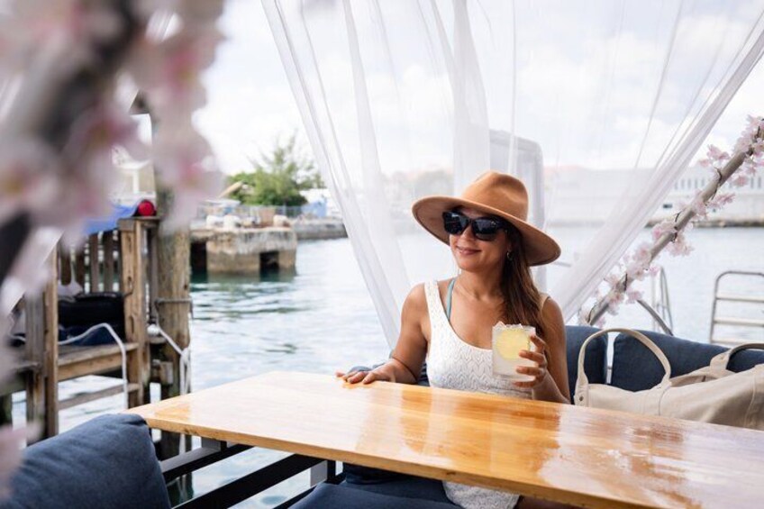 A person sitting at a wooden table on a boat, holding a drink. 4