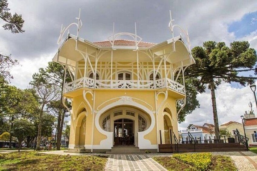 A yellow building with white balconies and arches, surrounded by trees and a paved walkway. 3