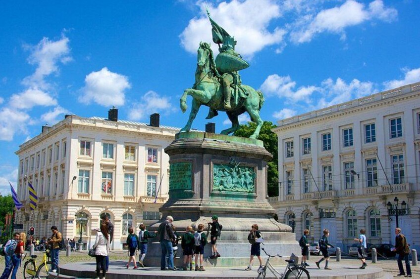A statue of a figure on horseback in a public square with buildings in the background. 1
