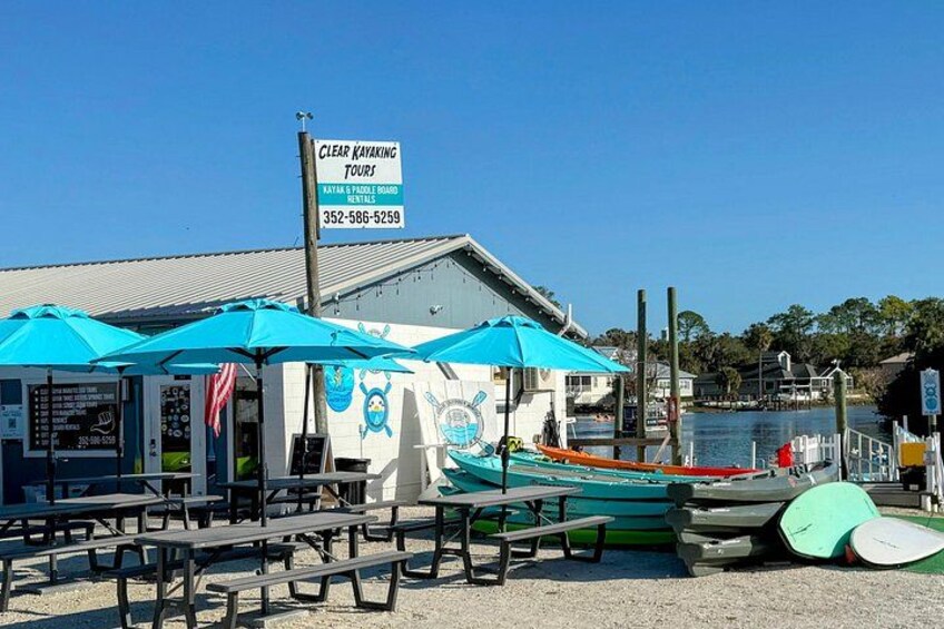 A clear kayaking tours sign, picnic tables, and kayaks at a waterfront location. 5