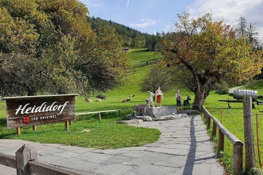 A sign for Heididorf, a pathway, and grazing cattle in a rural landscape. 4