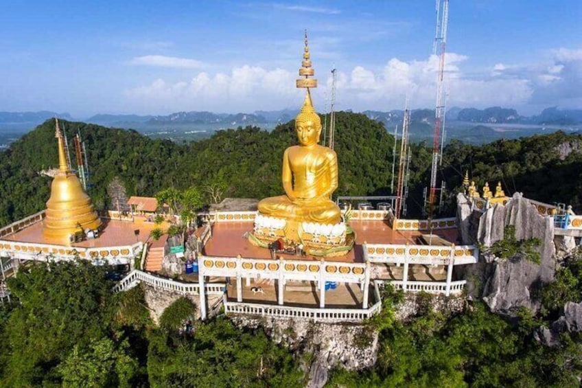 Eine große goldene Buddha-Statue, umgeben von kleineren goldenen Stupas, vor einer gebirgigen Kulisse. 1