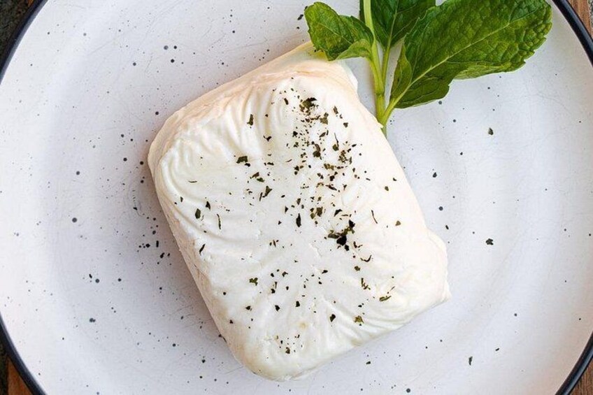 A block of white cheese garnished with herbs on a white plate. 4