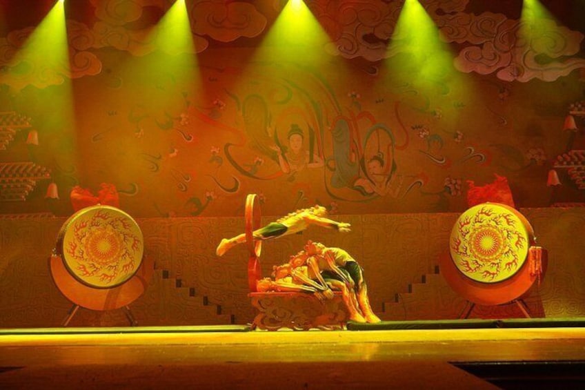 Una presentación tradicional con un artista en una plataforma elevada, rodeado de decoraciones elaboradas y un telón pintado. 2