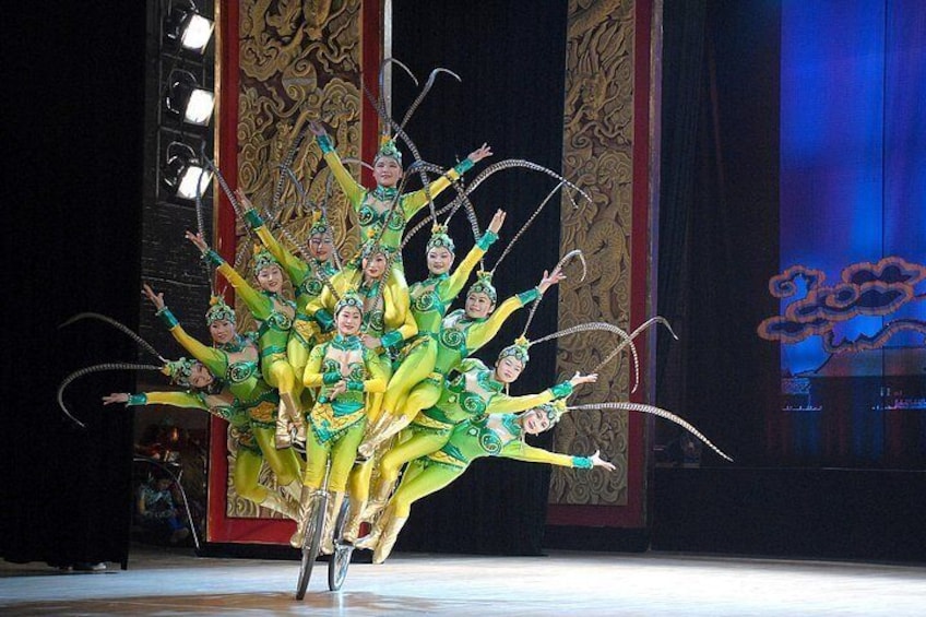 Un grupo de artistas con trajes verdes y detalles amarillos, actuando sobre un escenario ricamente decorado en rojo y dorado. 3