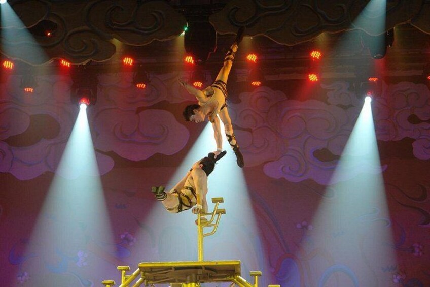 Un artista de circo equilibra un palo mientras otro artista cuelga de cabeza. 2