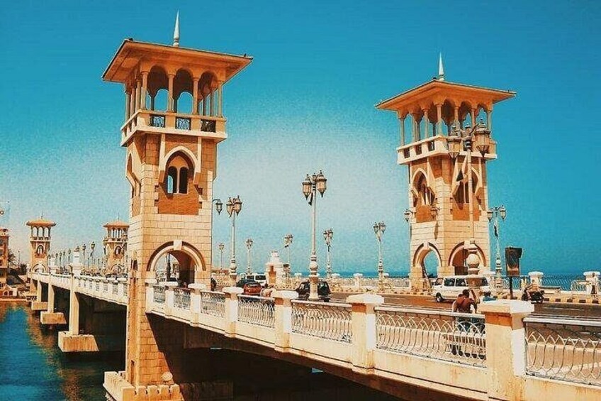 A bridge with two towers, a clear blue sky, and a calm body of water. 2