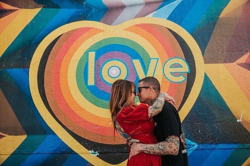 Et par omfavner foran en farverig mural med et hjerte og ordet 'love'. 3