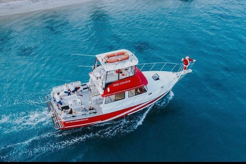 A red and white boat with a person in a Santa suit on the bow, moving through turquoise water. 3