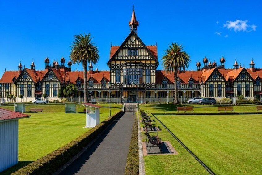 Un edificio grande e histórico con una torre destacada, rodeado de céspedes cuidados y palmeras. 5