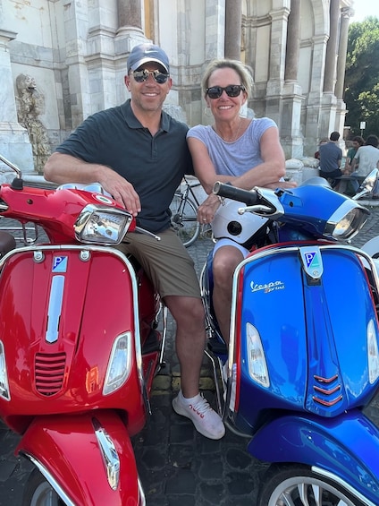 Kaksi ihmistä istuu vanhanaikaisten moottoriskoottereiden päällä historiallisesti merkittävän rakennuksen edessä. 5
