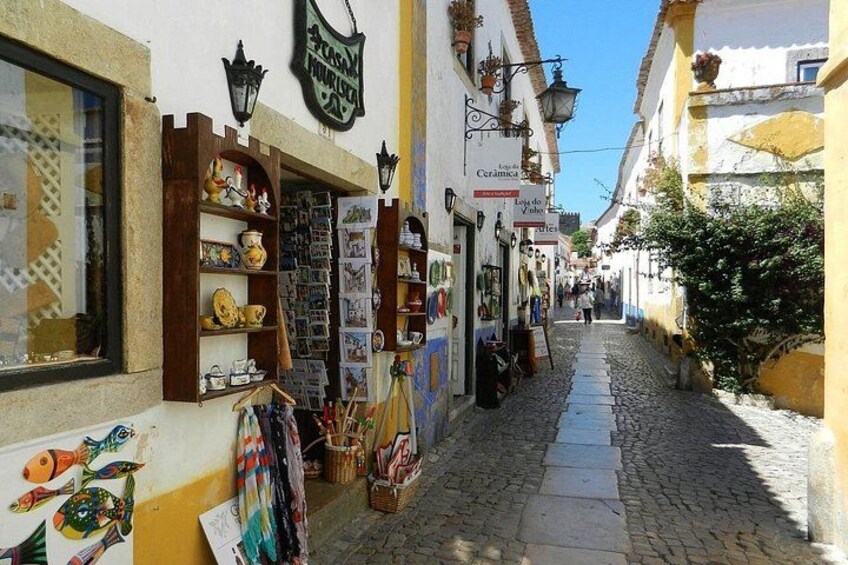 Una estrecha calle adoquinada con tiendas a ambos lados, incluyendo una tienda de cerámica y un comercio con artículos de colores. 2
