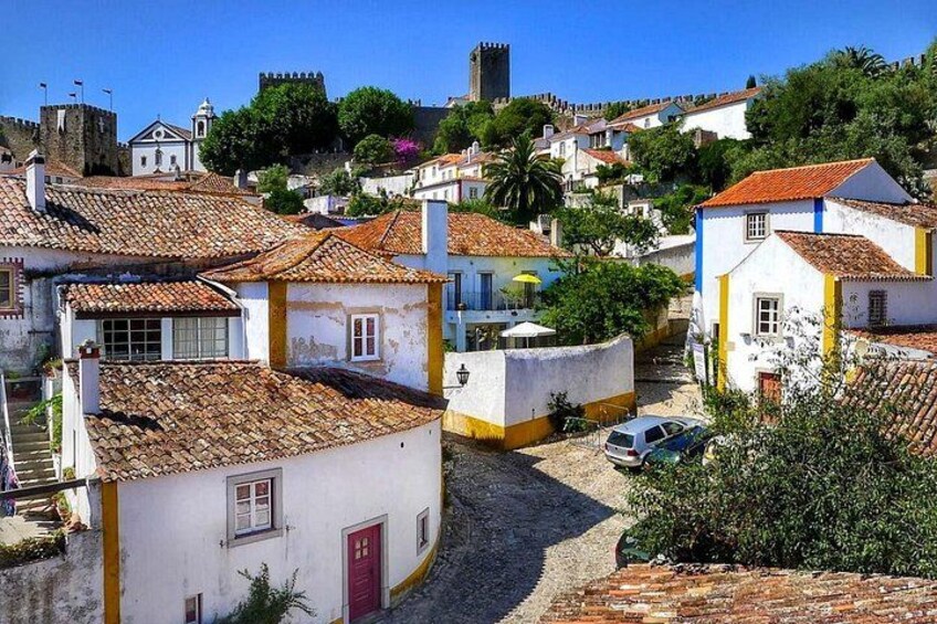 Una calle empedrada en un pueblo histórico con edificios blancos, una puerta roja y un castillo a lo lejos. 4