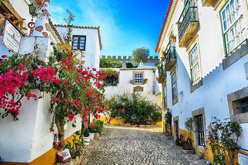 Una calle empedrada flanqueada por edificios blancos, con vibrantes flores de buganvilla y un cielo azul despejado. 3