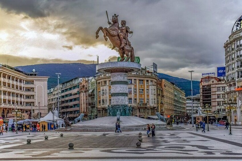 A public square with a large equestrian statue, surrounded by historic buildings and a mountainous backdrop. 4