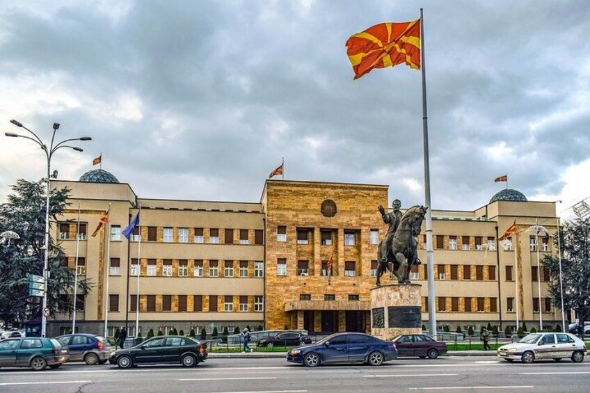 A government building with a flag, a statue, and multiple flags on poles. 5