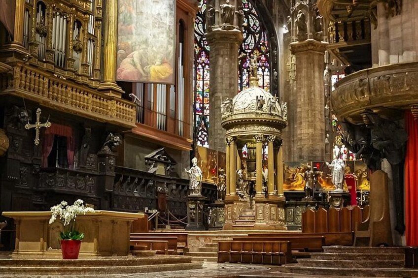 An ornate church interior with a central altar, stained glass windows, and religious statues. 5