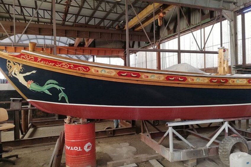 A boat with a mermaid design, in a workshop with tools and equipment. 4