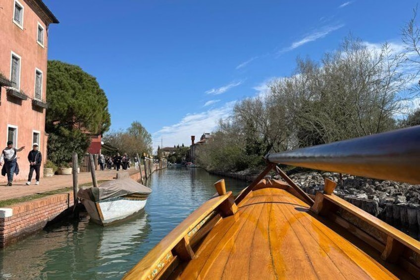 Ein hölzernes Boot auf einem Kanal, im Hintergrund Gebäude und Bäume. 2