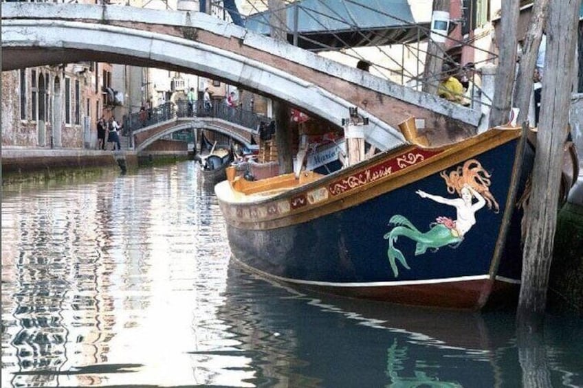 A boat with a mermaid design on its side, docked near a bridge over water. 2