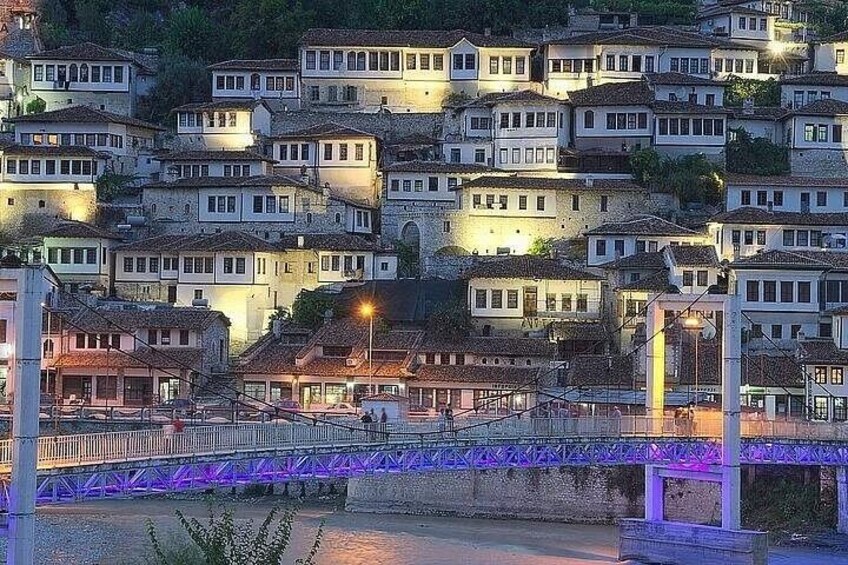 Un puente iluminado con luces moradas, un río y edificios en una colina. 2