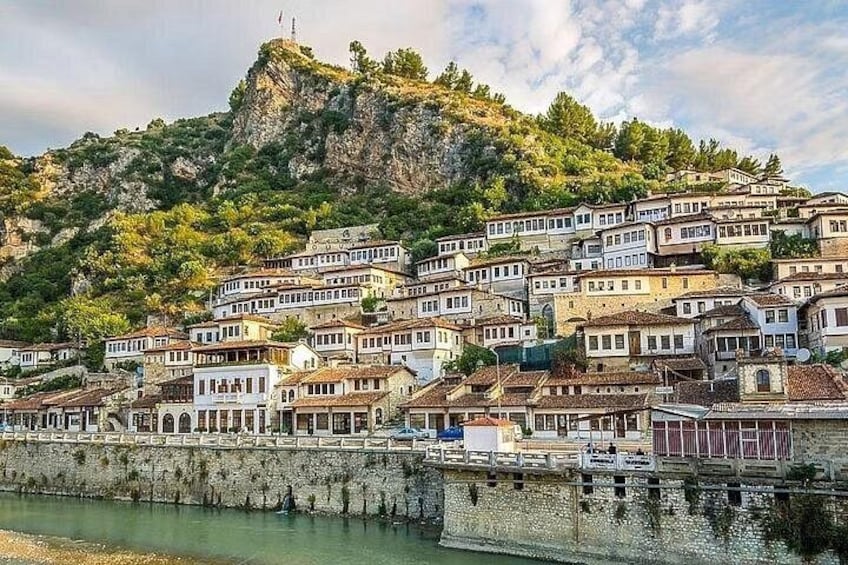 Un pueblo costero con edificios en una colina, una masa de agua al frente y un acantilado rocoso al fondo. 1