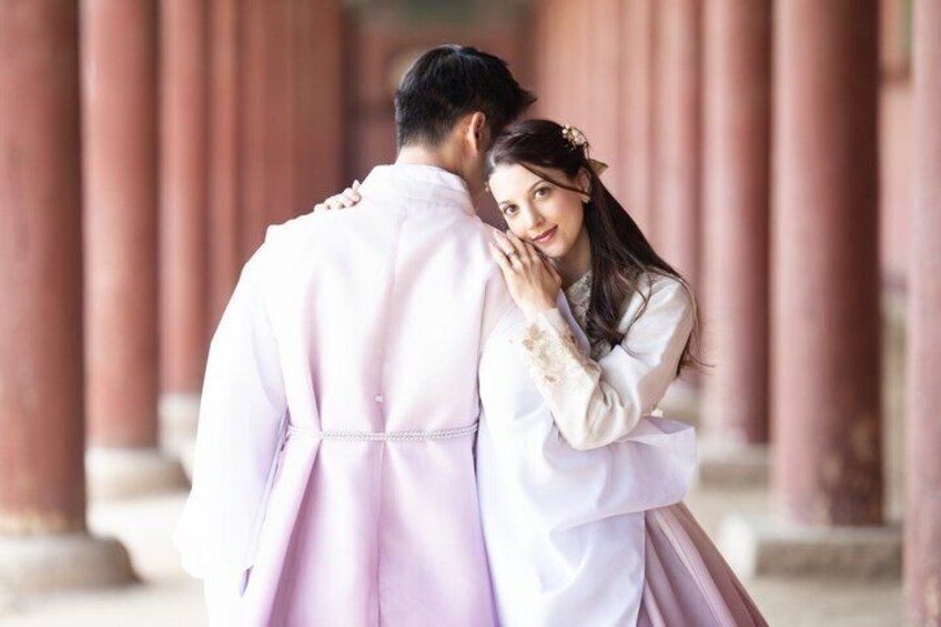 A couple in traditional attire standing in front of a row of red columns. 3