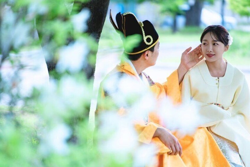 A person in traditional attire sitting outdoors with trees in the background. 5