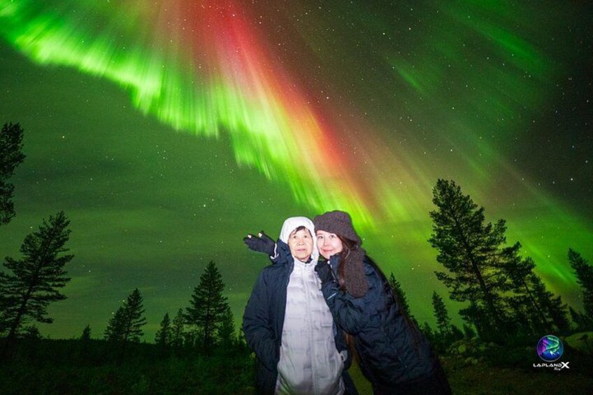To personer står i en skov under et grønt nordlys. 5