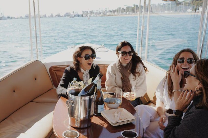 A group of people on a boat with a bottle of champagne and a glass of wine on the table. 1