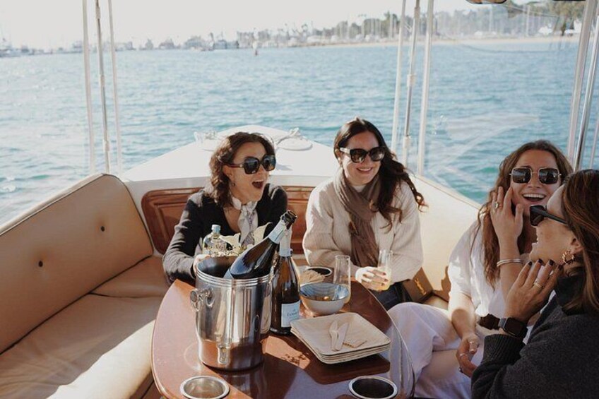 Un groupe de personnes se trouve sur un bateau, une bouteille de champagne et un verre de vin sont posés sur la table. 4