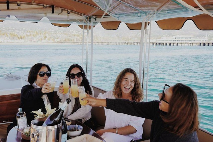 A group of people toasting with drinks on a boat, with water and a pier in the background. 2