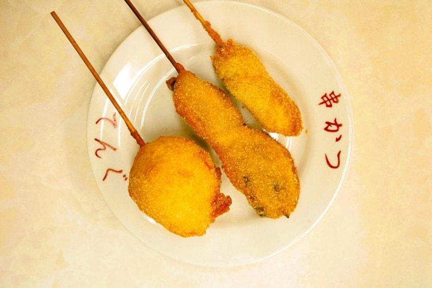 Tre corn dogs på spyd på en tallerken med japansk tekst. 2