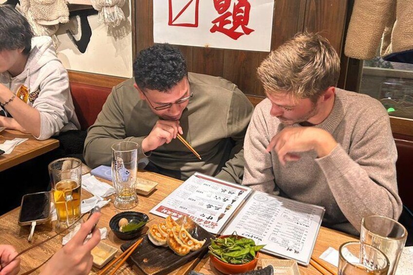 Tre personer spiser på en restaurant med en menu, spisepinde og en skål mad. 2